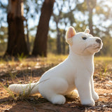 White plush dingo toy in a natural setting with trees and grass.
