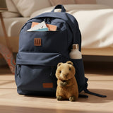 Mini quokka plush toy beside navy backpack on wooden floor.
