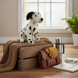 Pebbles Dalmatian plush sitting on wooden crate with blanket and travel gear.