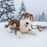 Scarlet Husky plush toy lying in snowy forest beside wooden sled.