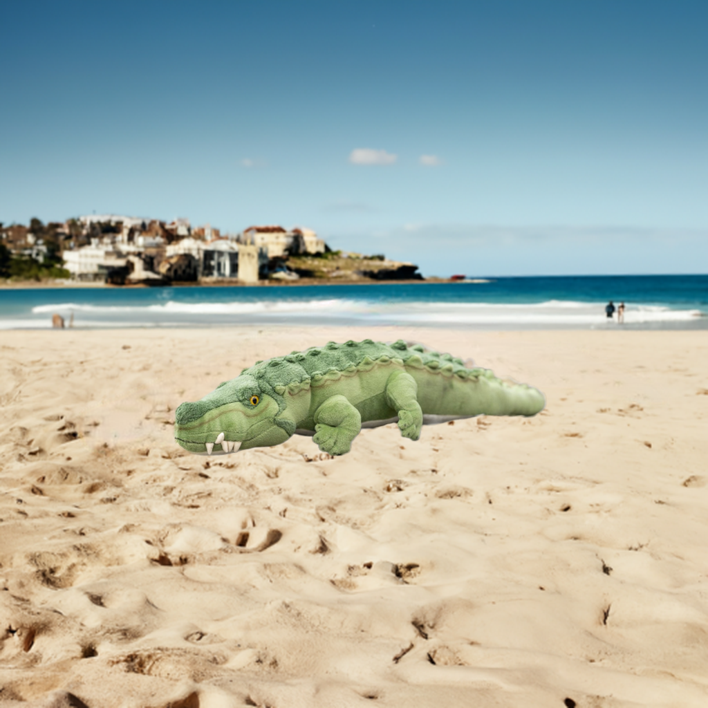 A large, green crocodile plush toy specifically the 80cm Agro Crocodile from Bocchetta Plush Toys lies on a sandy beach.