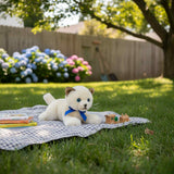 Bamboo Siamese kitten plush toy with blue ribbon lying on checkered blanket outdoors beside books and toy houses.