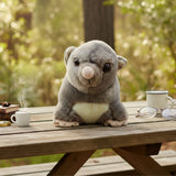 Mini possum plush toy on picnic table with coffee and glasses.