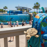Mini turtle plush toy keychain on a backpack at outdoor aquarium.