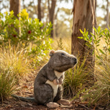 A plush potoroo toy with realistic grey and brown fur sits upright in a sunlit, grassy outdoor setting.