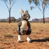 Stuffed wombat toy in a desert landscape with trees and mountains in the background