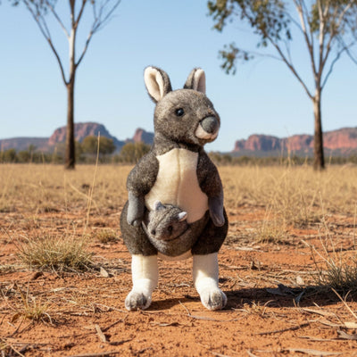 Stuffed wombat toy in a desert landscape with trees and mountains in the background