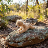 Plush toy thylacine lying on a rock in a natural setting with trees and plants.