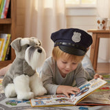 Child wearing police hat reading book beside Watson Schnauzer plush toy in a room